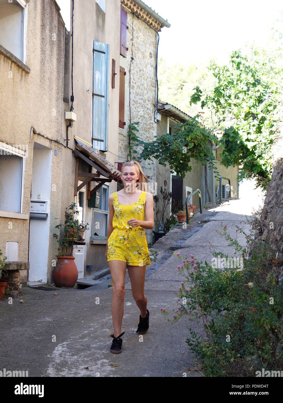 Eine fröhliche und hell gekleidet 16 jährige Blonde Mädchen auf einem Hügel durch die alten Straßen des Dorfes von Cessenon, in Richtung der Kamera Stockfoto