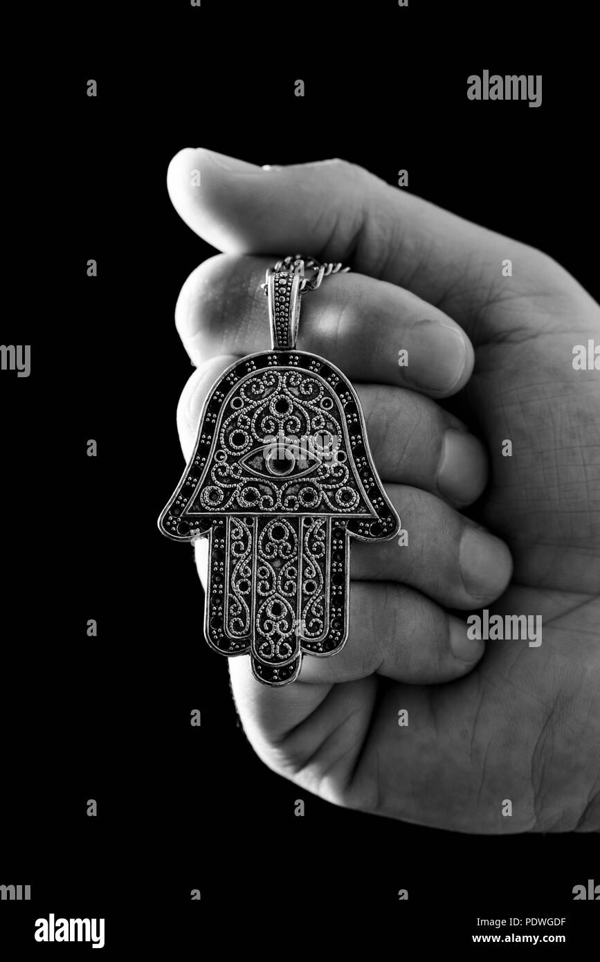 Nahaufnahme der Hand eines jungen Mannes mit einem alten hamsa Amulett, auch bekannt von der Hand der Fatima oder der Hand Mariens, in Schwarz und Weiß Stockfoto