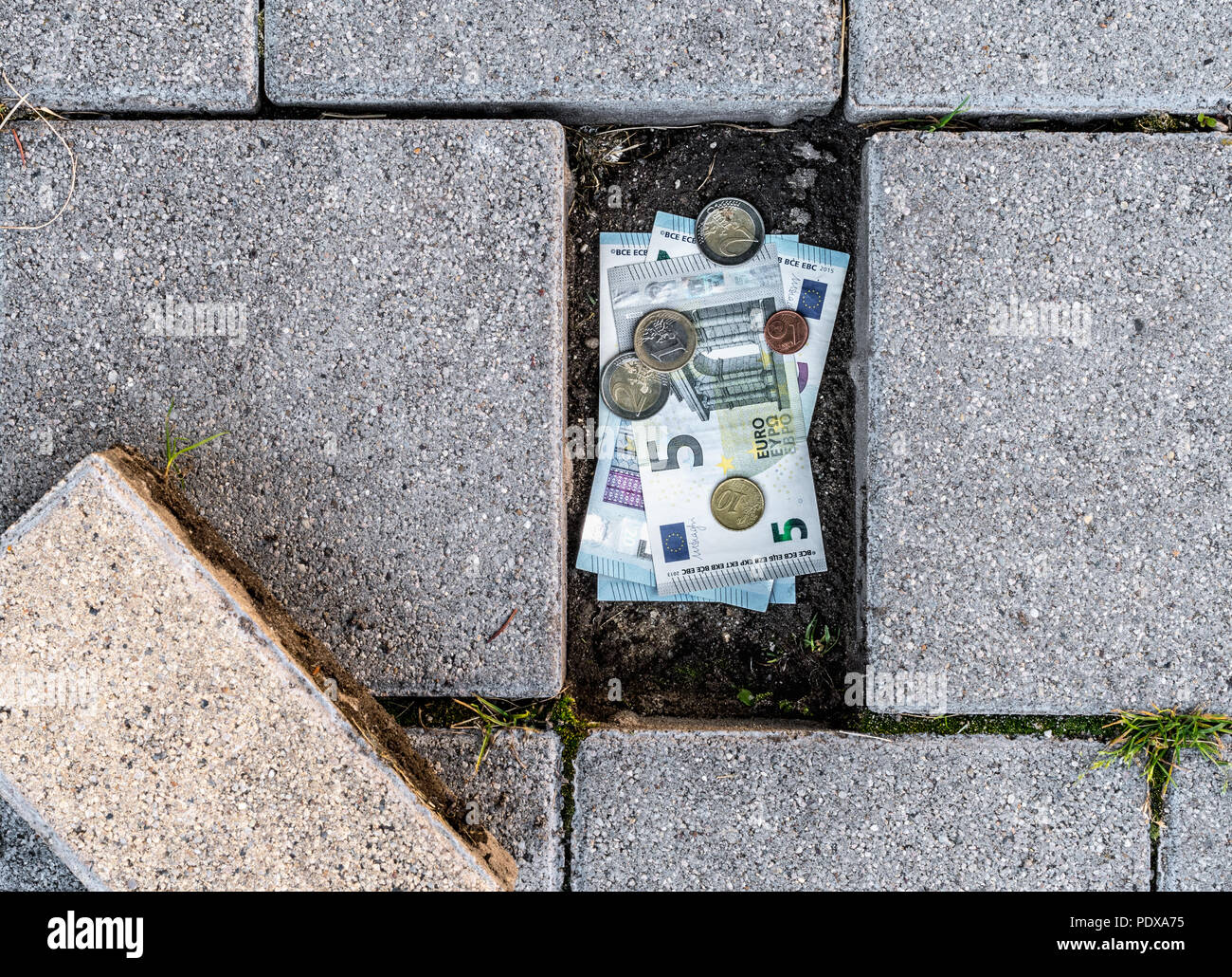 Euro-banknoten und -Münzen unter einem lose Pflaster Ziegel gefunden. Konzept des Laufens aus persönlichen Ersparnissen Stockfoto