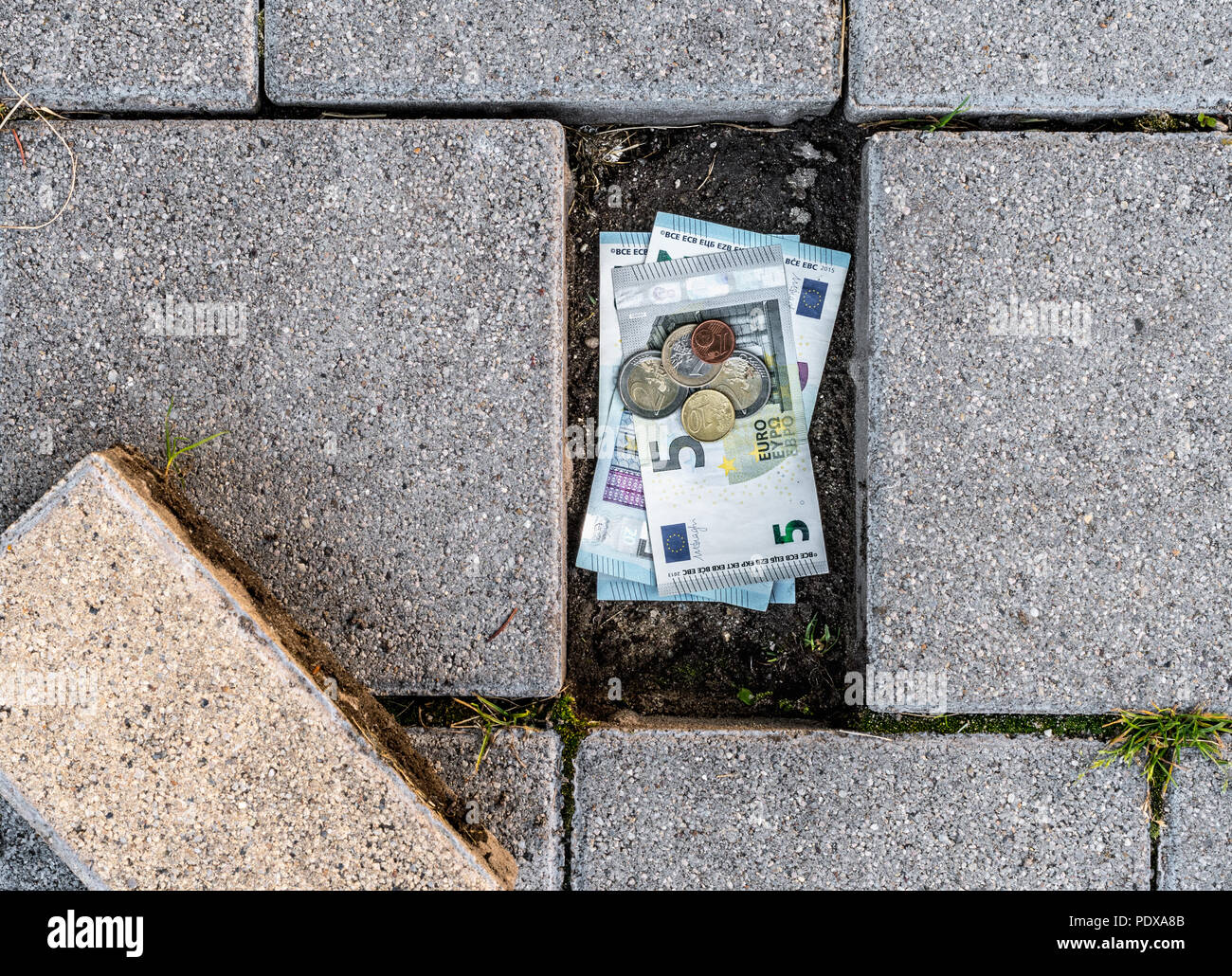 Euro-banknoten und -Münzen unter einem lose Pflaster Ziegel gefunden. Konzept des Laufens aus persönlichen Ersparnissen Stockfoto