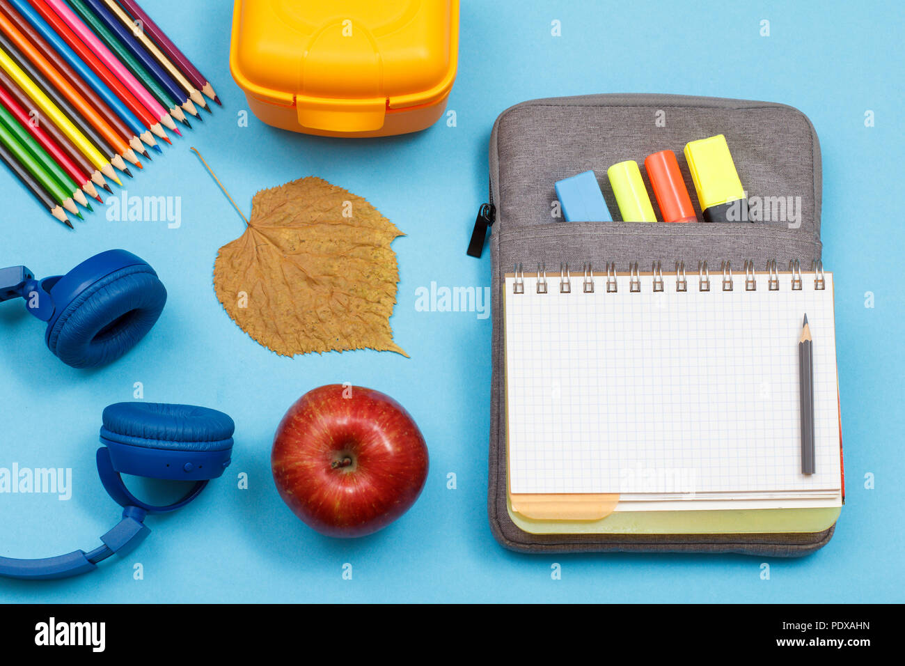 Kopfhörer, Buntstifte, Apple, trockene Blätter, Lunchbox, Öffnen Sie dazu die Übung Buch auf Tasche - Federmäppchen mit Farbe filzstifte und Marker auf blauem Hintergrund. Nach oben V Stockfoto