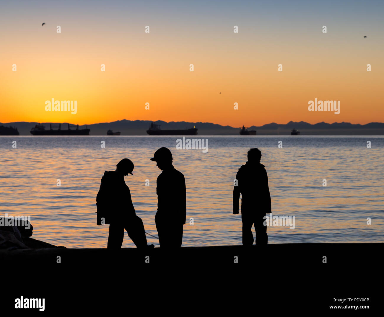 Drei Kinder mit Blick über das Wasser in Richtung Sonnenuntergang. Stockfoto