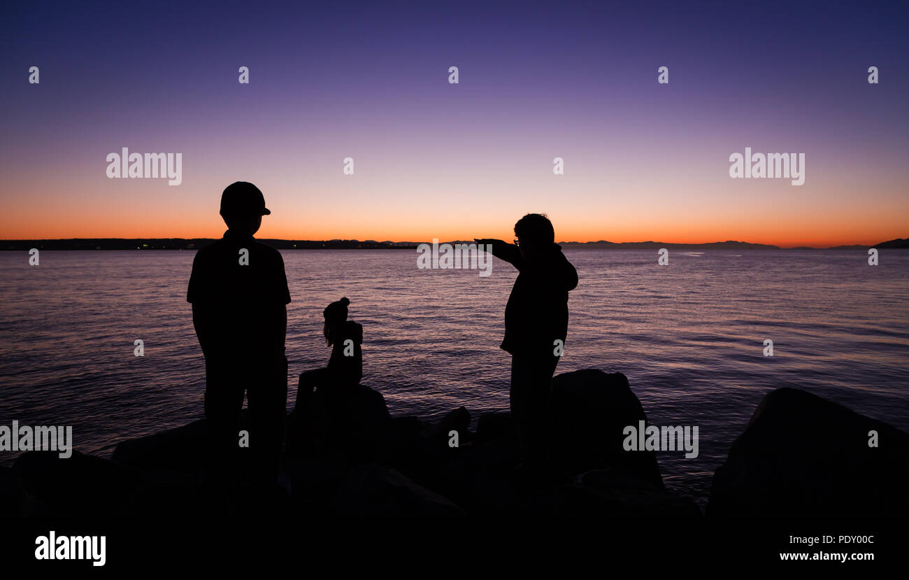 Drei Kinder mit Blick über das Wasser in Richtung Sonnenuntergang. Stockfoto
