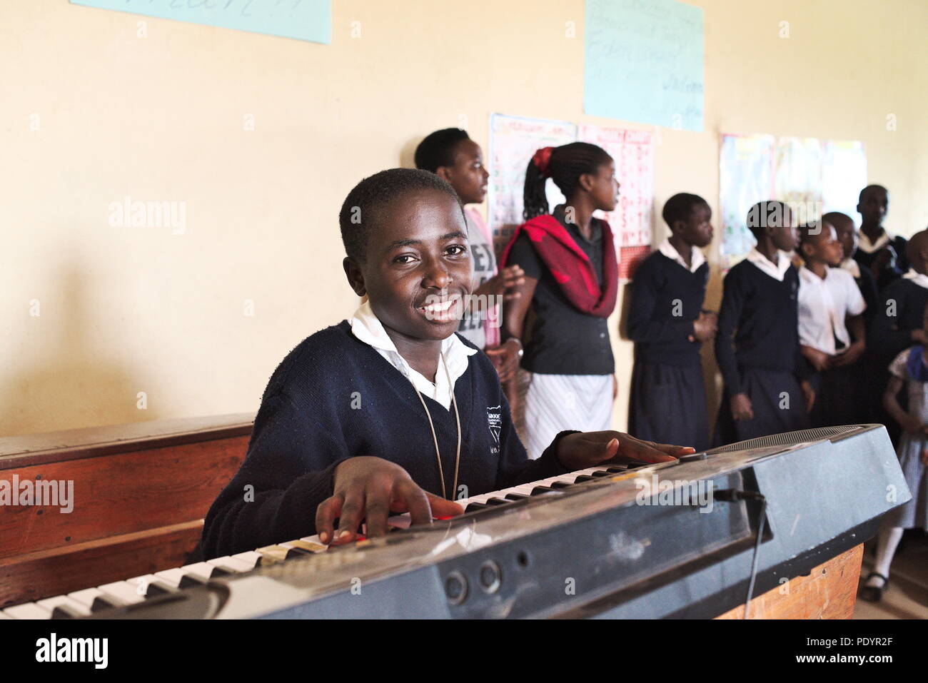 Junges ugandisches Mädchen lächelt an der Kamera, während es in der Schulversammlung eine Tastatur spielt Stockfoto