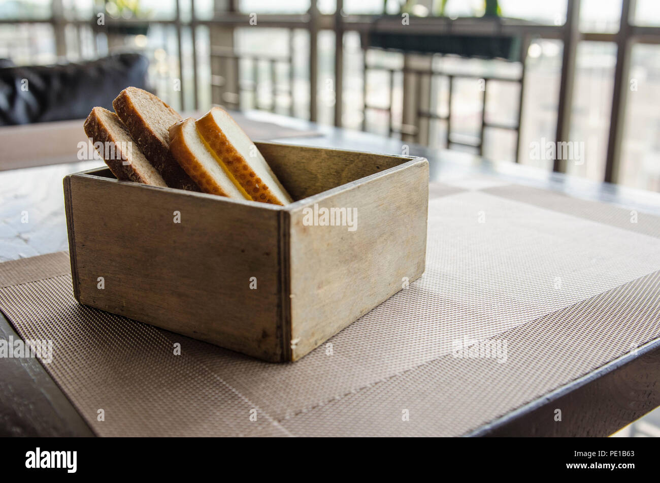 In Holz geschnitten Brot Brot Box. Vier Stücke Brot in einem schönen breadbox auf einem Tisch in einem Café. Frisches Brot in Holz- Brot Box mit Hintergrund Stockfoto