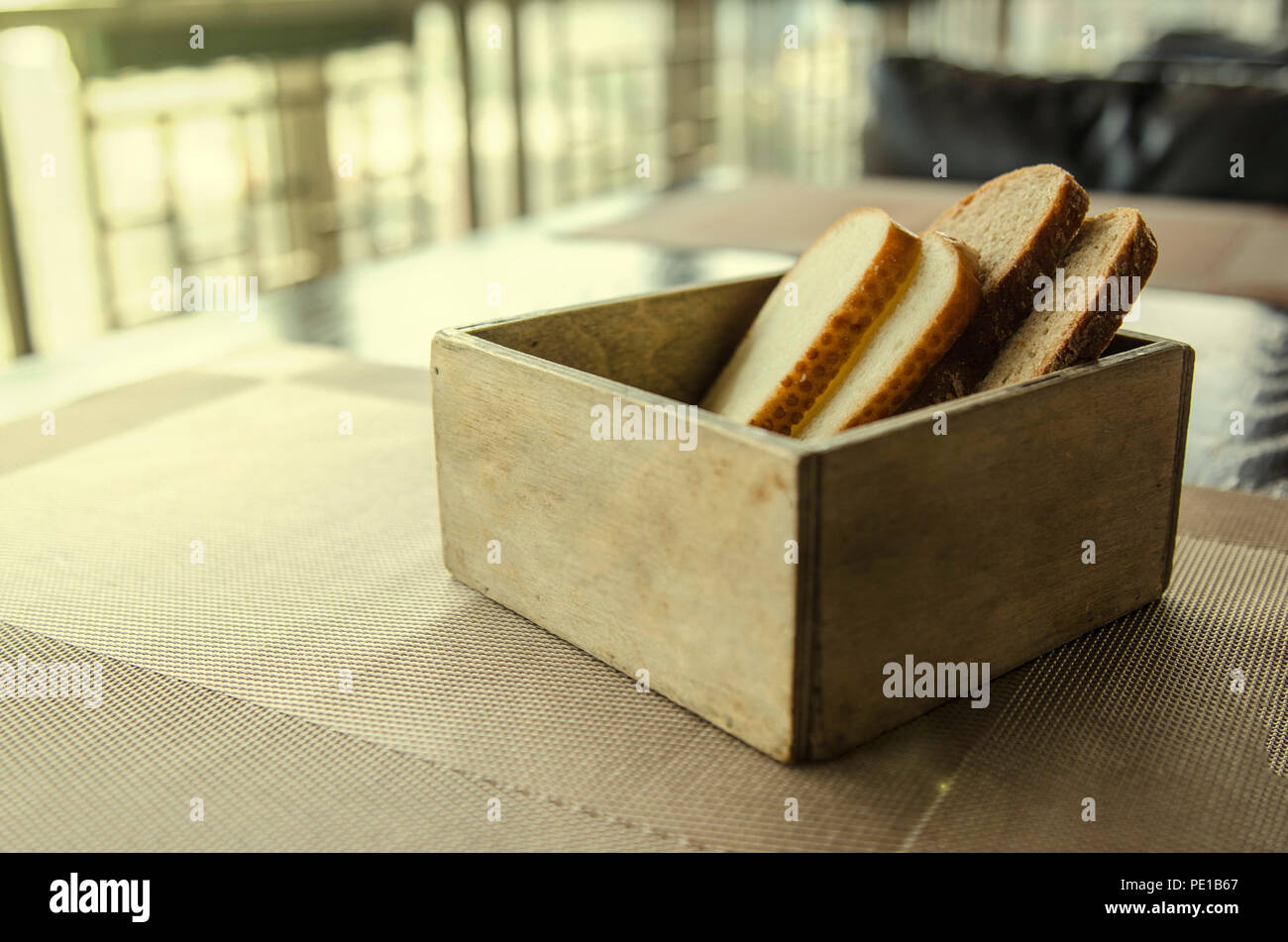 In Holz geschnitten Brot Brot Box. Vier Stücke Brot in einem schönen breadbox auf einem Tisch in einem Café. Frisches Brot in Holz- Brot Box mit Hintergrund Stockfoto