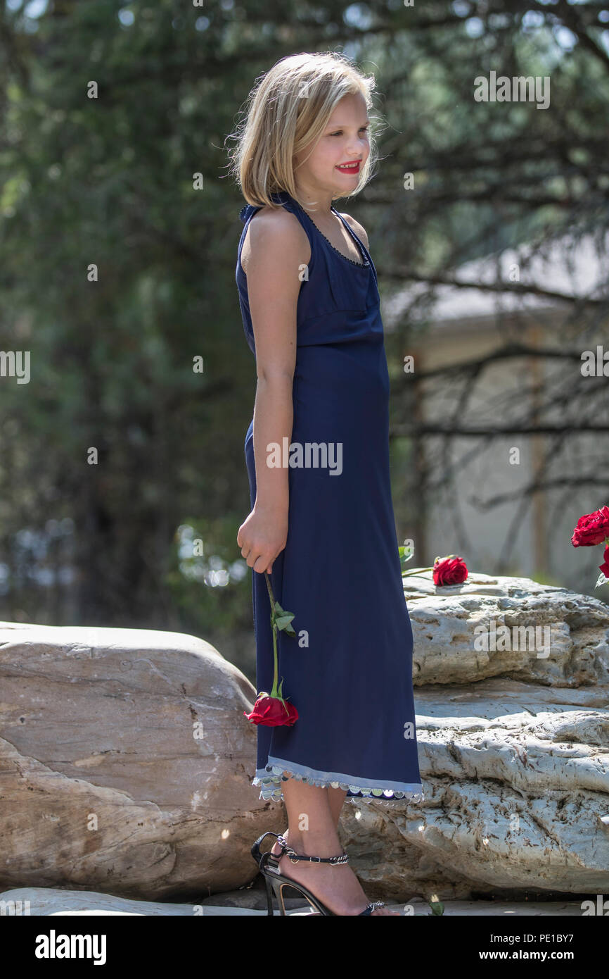 Hübsche, junge blonde Frau. preteenn, Mode schießen. Standing Rock, mit einer roten Rose in der Hand. 3/4 Profil, blaues Kleid, Model Released. Stockfoto