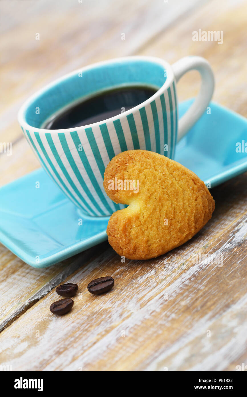 Herzförmige crunchy Cookie lehnte sich gegen blaue Tasse Kaffee auf Holzmöbeln im Landhausstil Oberfläche Stockfoto