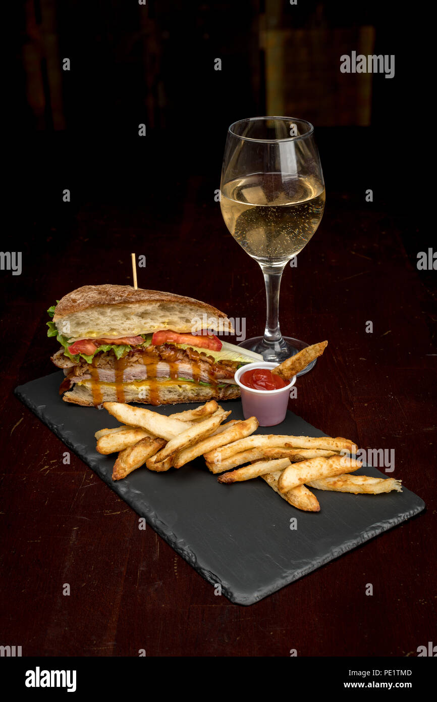 Mittag- Server auf einem Schiefer Platte iwht ein schönes Glas jammern mit Pommes und einem Club Stockfoto