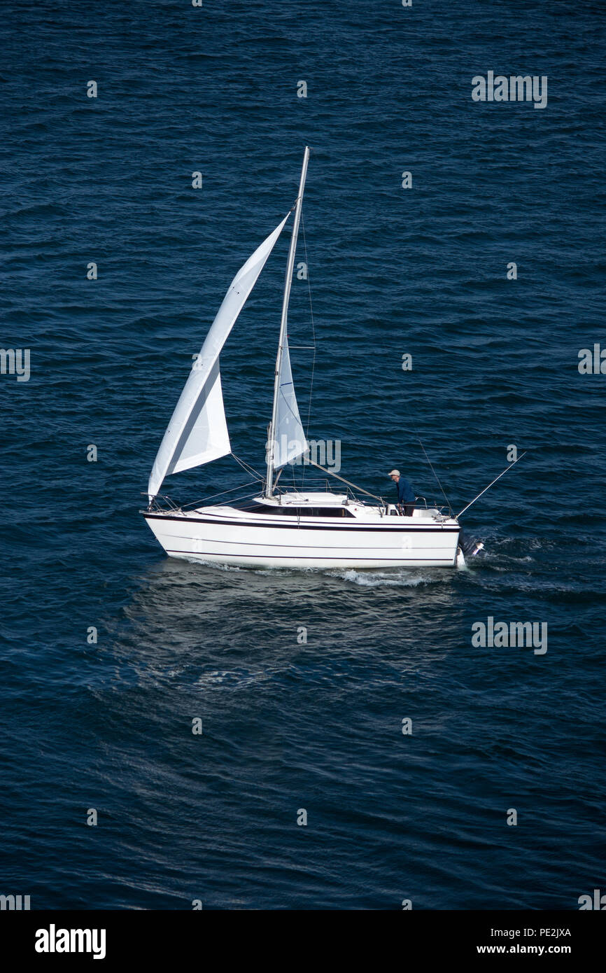 Solo sailor in kleinen Segelboot auf blaues Wasser mit Reflexion der weißen Segel Stockfoto