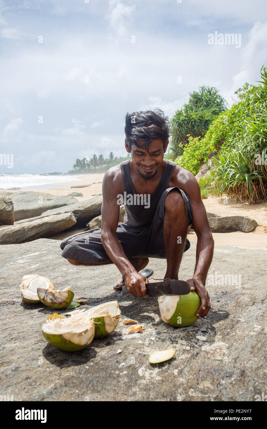 Junger Mann hacken eine Kokosnuss am Strand. Ambalangoda 29. Mai 20. Stockfoto