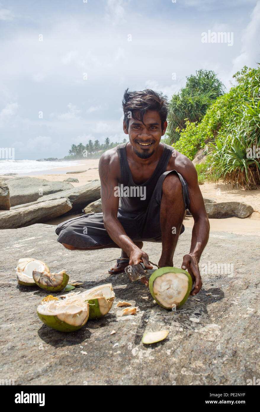 Junger Mann hacken eine Kokosnuss am Strand. Ambalangoda 29. Mai 20. Stockfoto