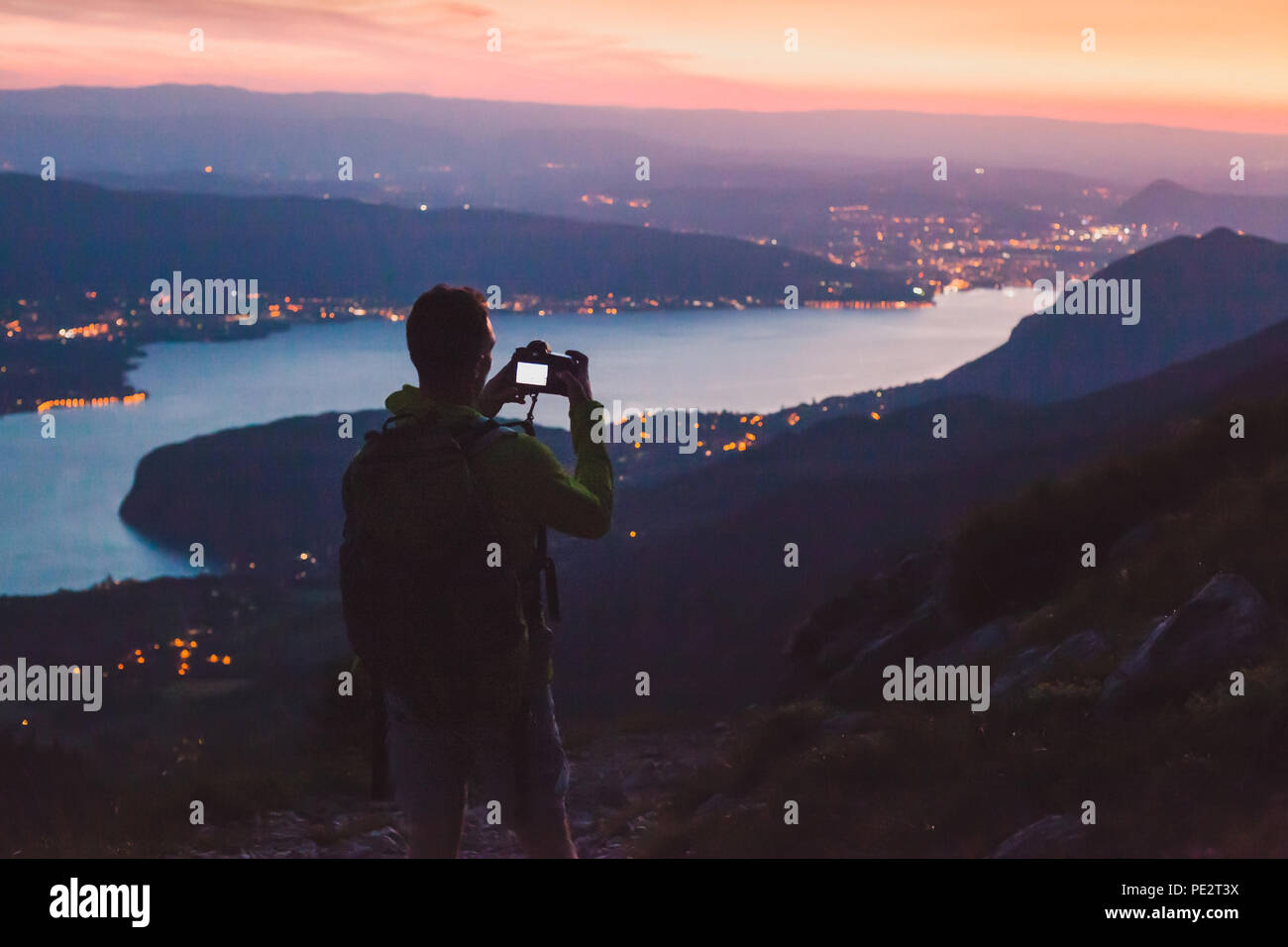 Fotograf, Foto auf DSLR-Kamera am Abend nach Sonnenuntergang Dämmerung, Stadt Panoramablick auf die Berglandschaft low light, Dämmerung Stockfoto