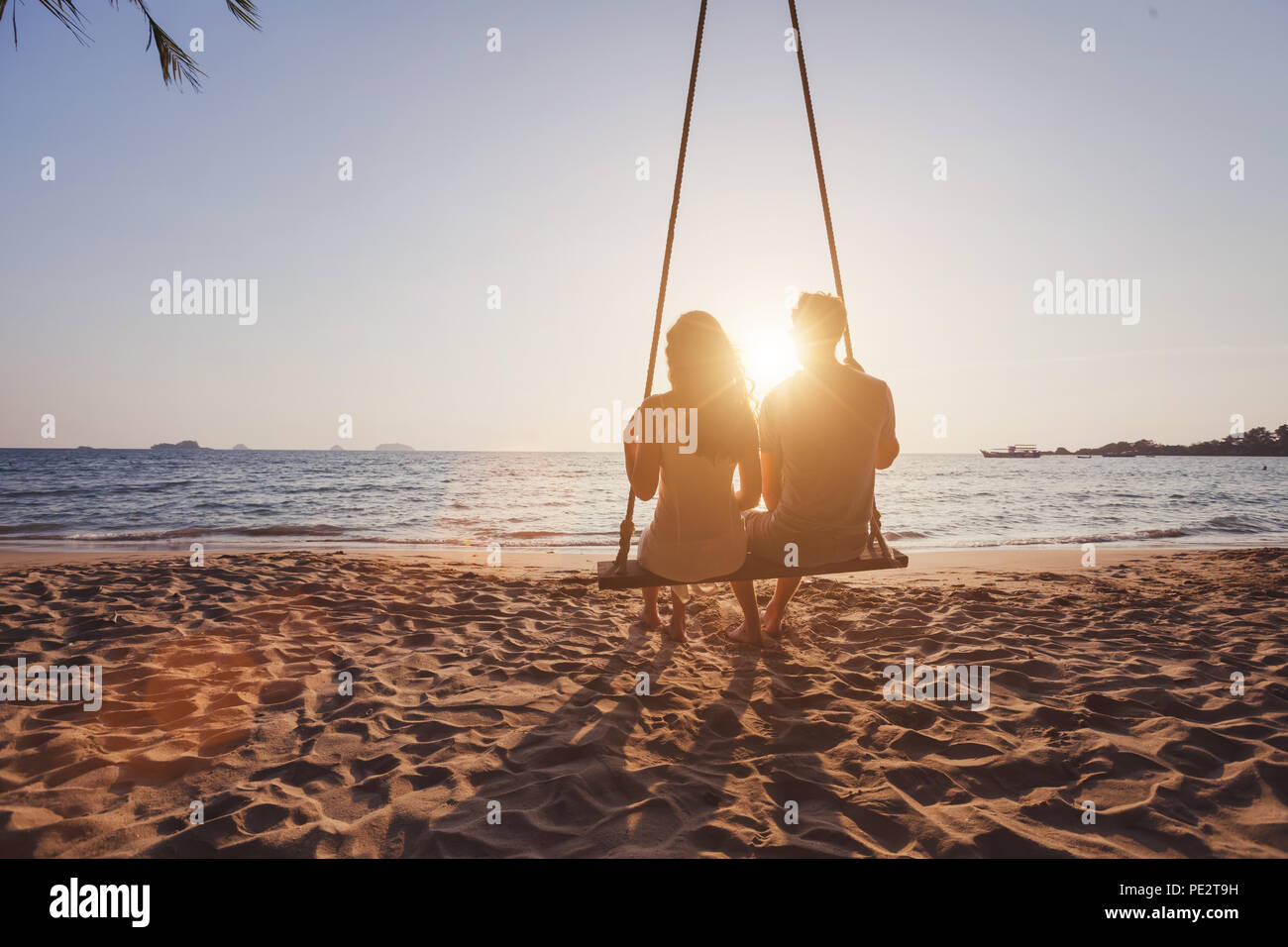Urlaub am Meer für romantische junges Paar, Hochzeitsreise Urlaub, Silhouetten von Mann und Frau sitzen zusammen auf Swing und Sonnenuntergang Stockfoto
