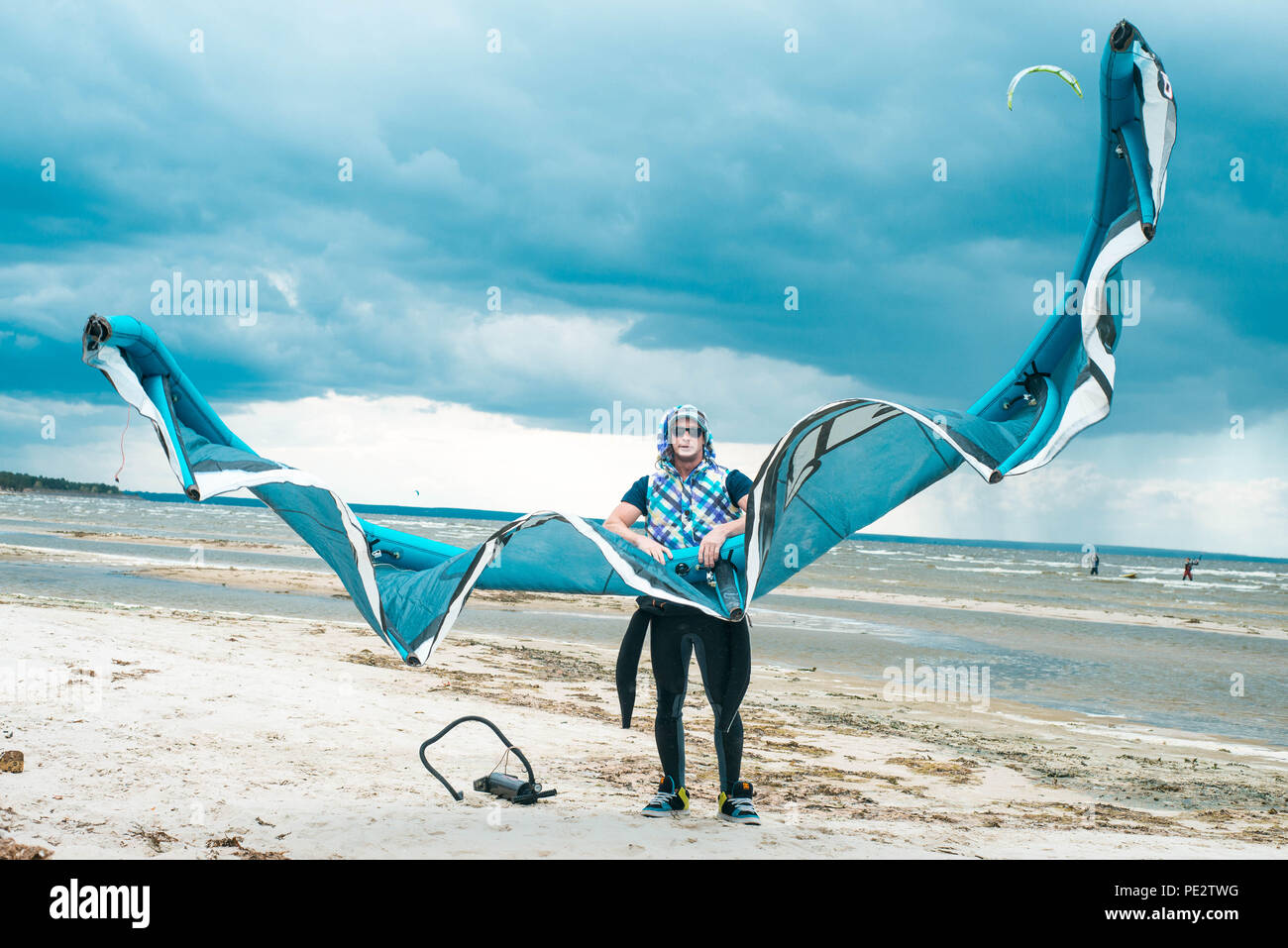 Kitesurfer hält seinen Drachen mit einem Sturm im Hintergrund in einem schönen symmetrischen Porträt. Kite Surfer hält Kite an einem Strand bei stürmischem Wetter Stockfoto