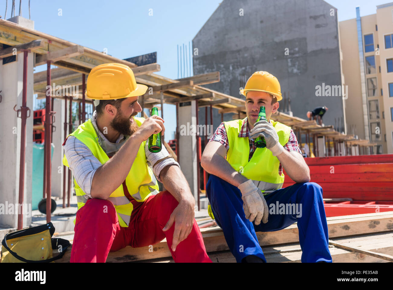 Zwei junge Arbeiter trinken ein kaltes Bier in der Pause bei der Arbeit Stockfoto