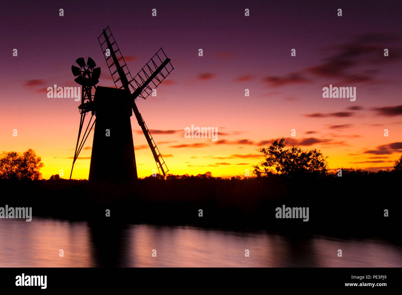 Rasen Fen Windmühle auf den Norfolk Broads gegen einen roten Abendhimmel. Stockfoto