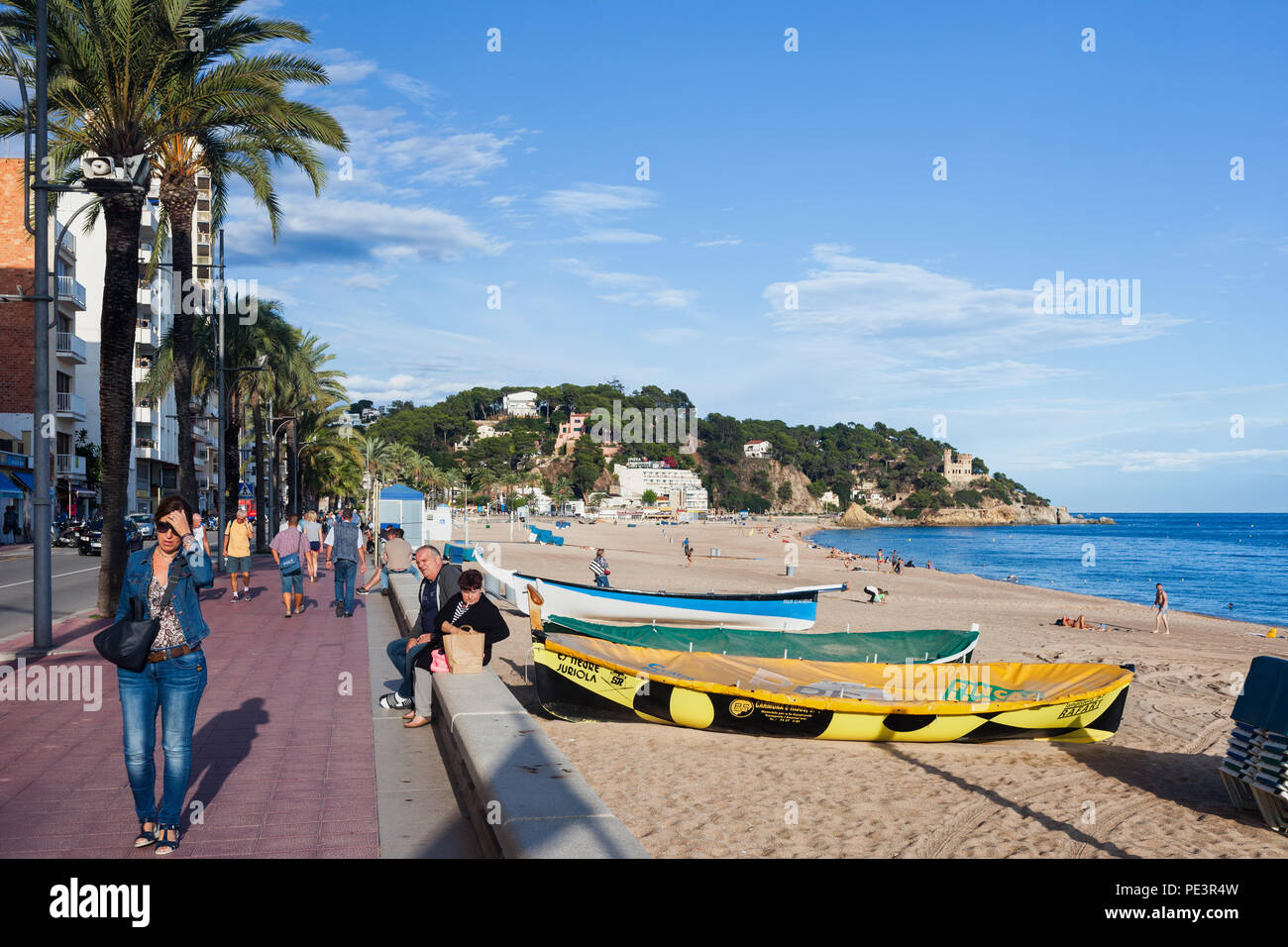 Lloret de Mar Badeort an der Costa Brava in Katalonien, Spanien, Leute auf die Strandpromenade mit Palmen gesäumt, Boote am Strand am Mittelmeer Stockfoto