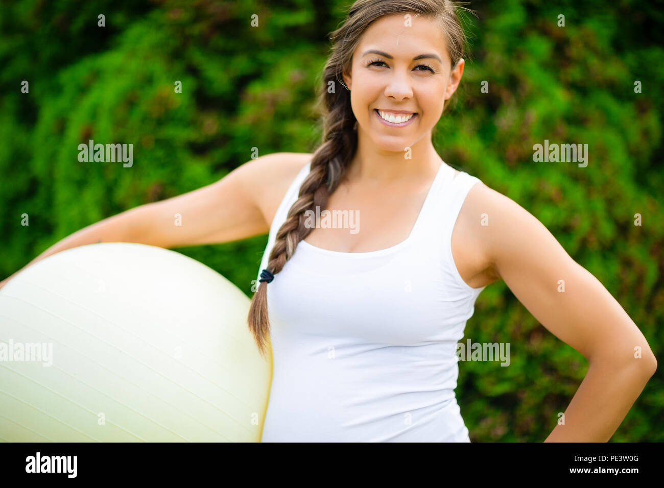Lächelnde junge schwangere Frau mit Fitness Ball im Park Stockfoto