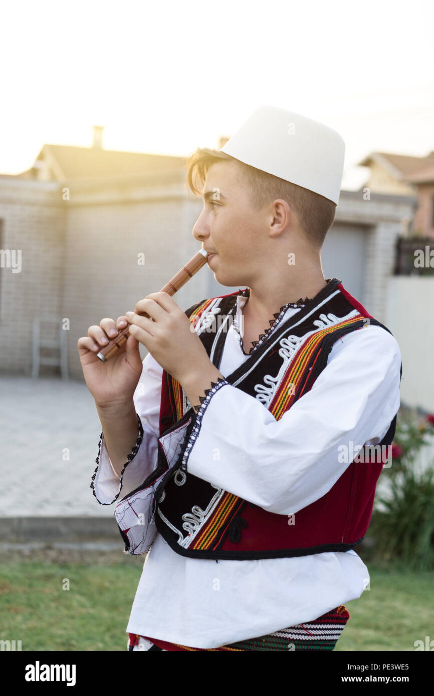 Junge Mann in der traditionellen albanischen Kostüm spielt Flöte vor der Natur Wiese und Abenddämmerung Stockfoto