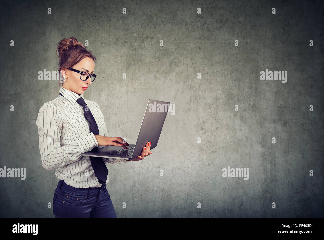 Professionelle Frau in formalen Outfit und Gläser mit Laptop und gegen graue Wand Hintergrund Stockfoto