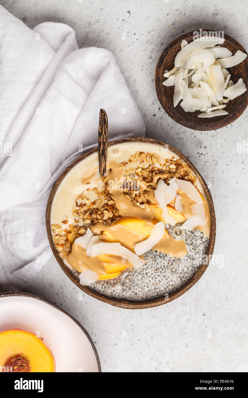 Smoothie Schüssel mit Chia Pudding, Pfirsich, Kokosnuss und Müsli in eine Kokosnuss  Schale auf weißem Hintergrund, Ansicht von oben. Vegan gesundes Frühstück,  sauber essen Conc Stockfotografie - Alamy