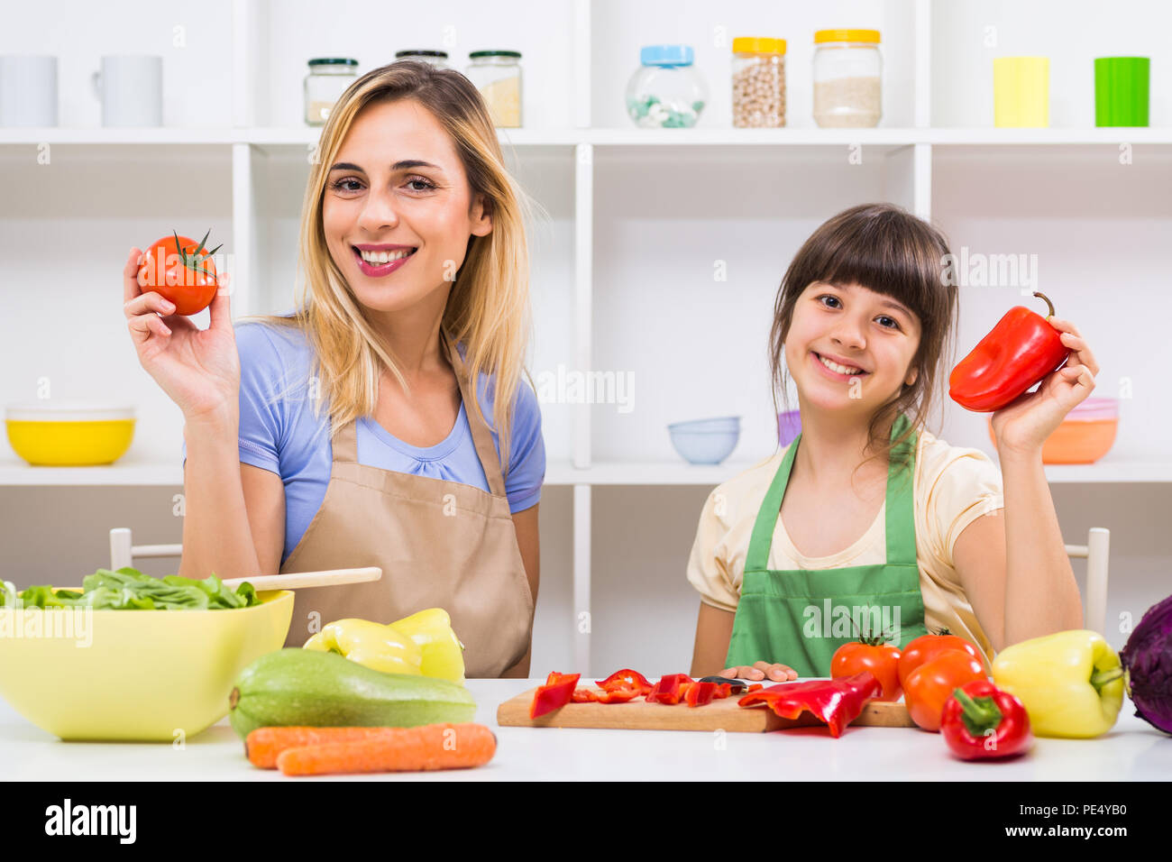 Glückliche Mutter und ihrer Tochter mit Tomaten und Paprika, während Sie genießen Sie gesunde Mahlzeit zusammen, an ihrem Haus. Stockfoto