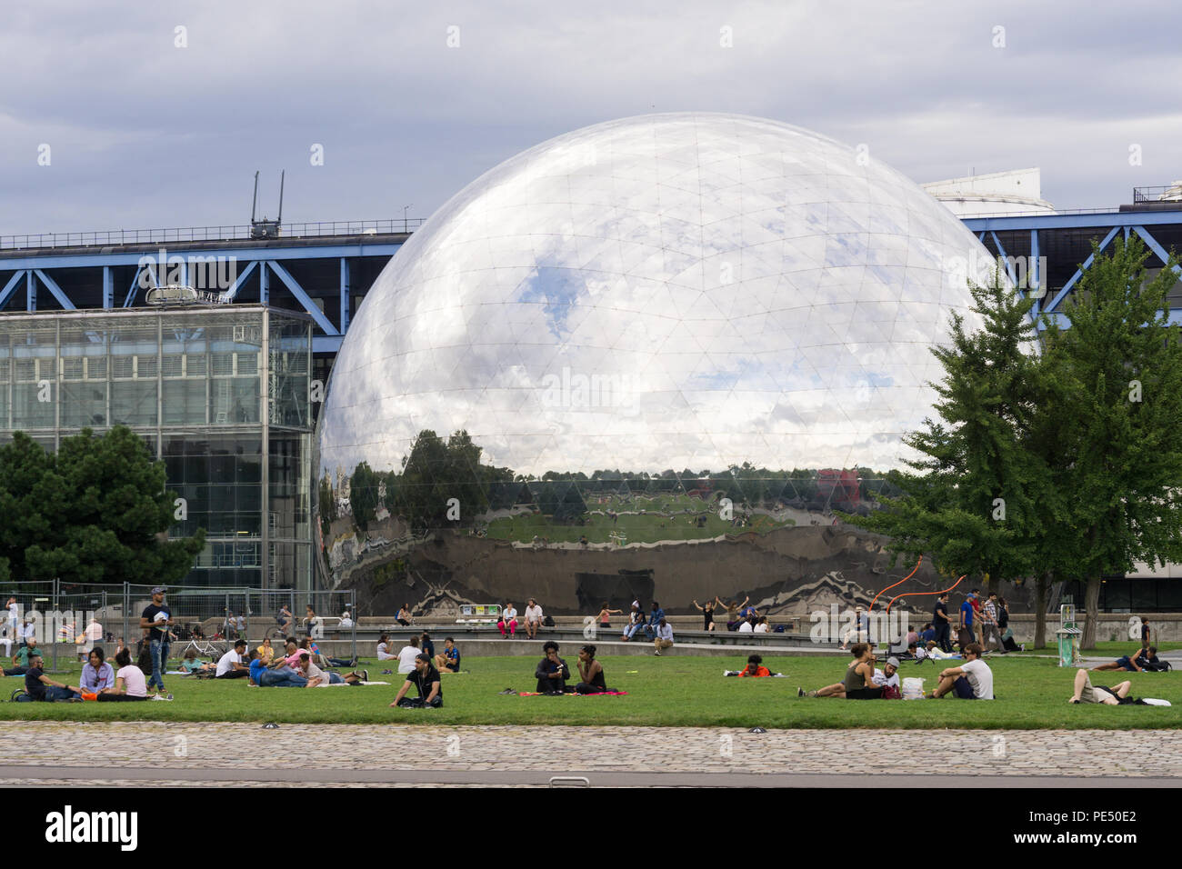Paris Park - Menschen entspannend auf Gras der Park La Villette mit Blick auf Spiegel- dome La Géode, Paris, Frankreich, Stockfoto