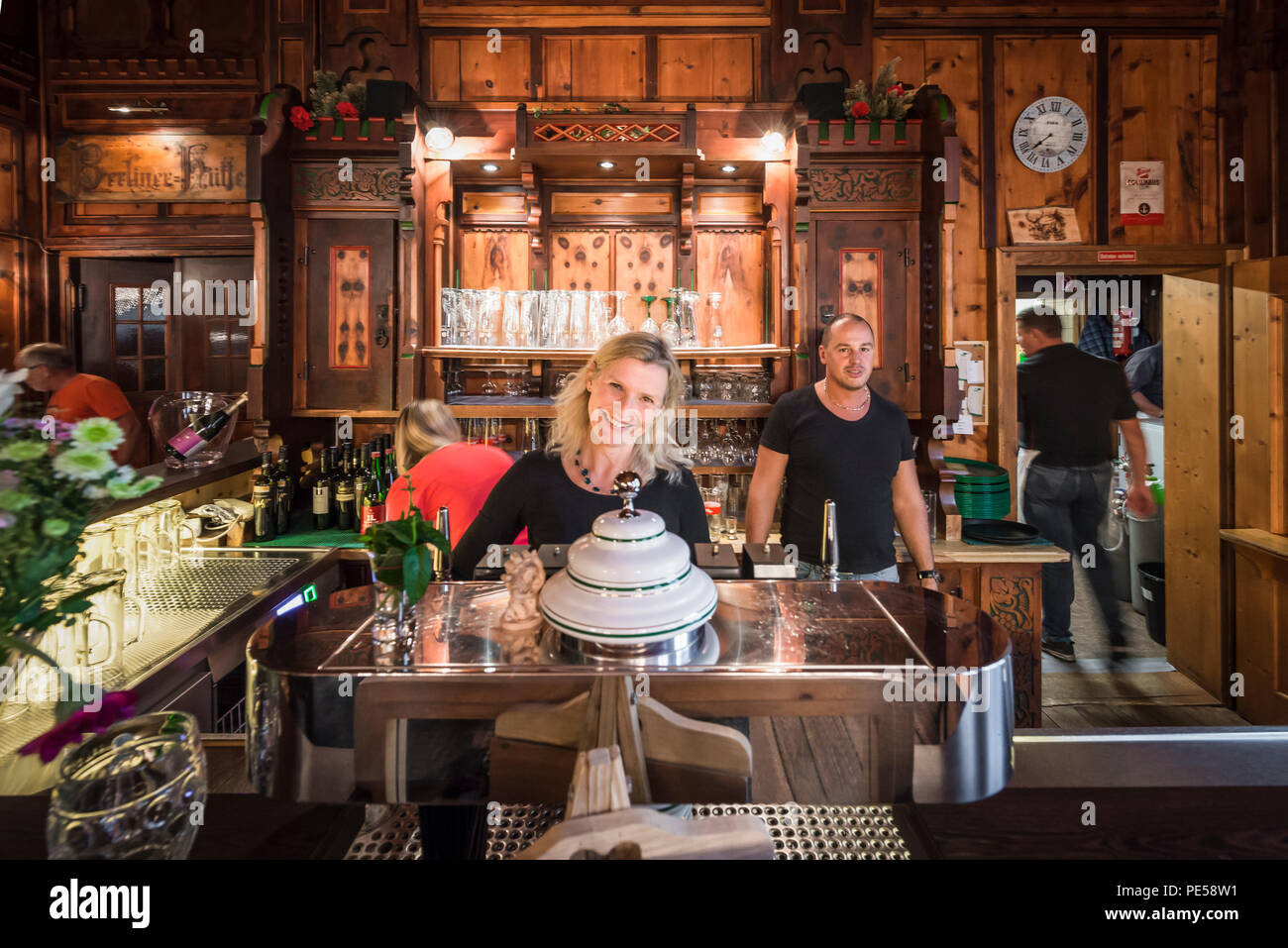 Blonde Frau und Mann hinter der Theke in der herrlichen Speisesaal der Berghütte Berliner Hütte lächeln in die Kamera, Zillertal, Österreich Stockfoto