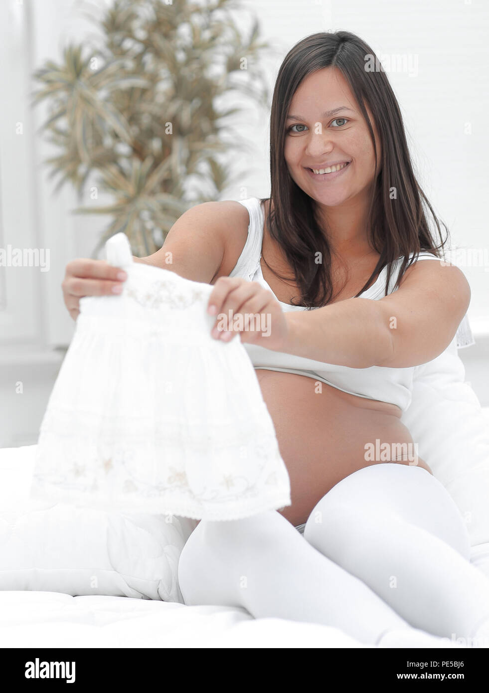 Schwangere Frau angesichts der Kinder T-Shirt, auf dem Bett zu sitzen. Stockfoto