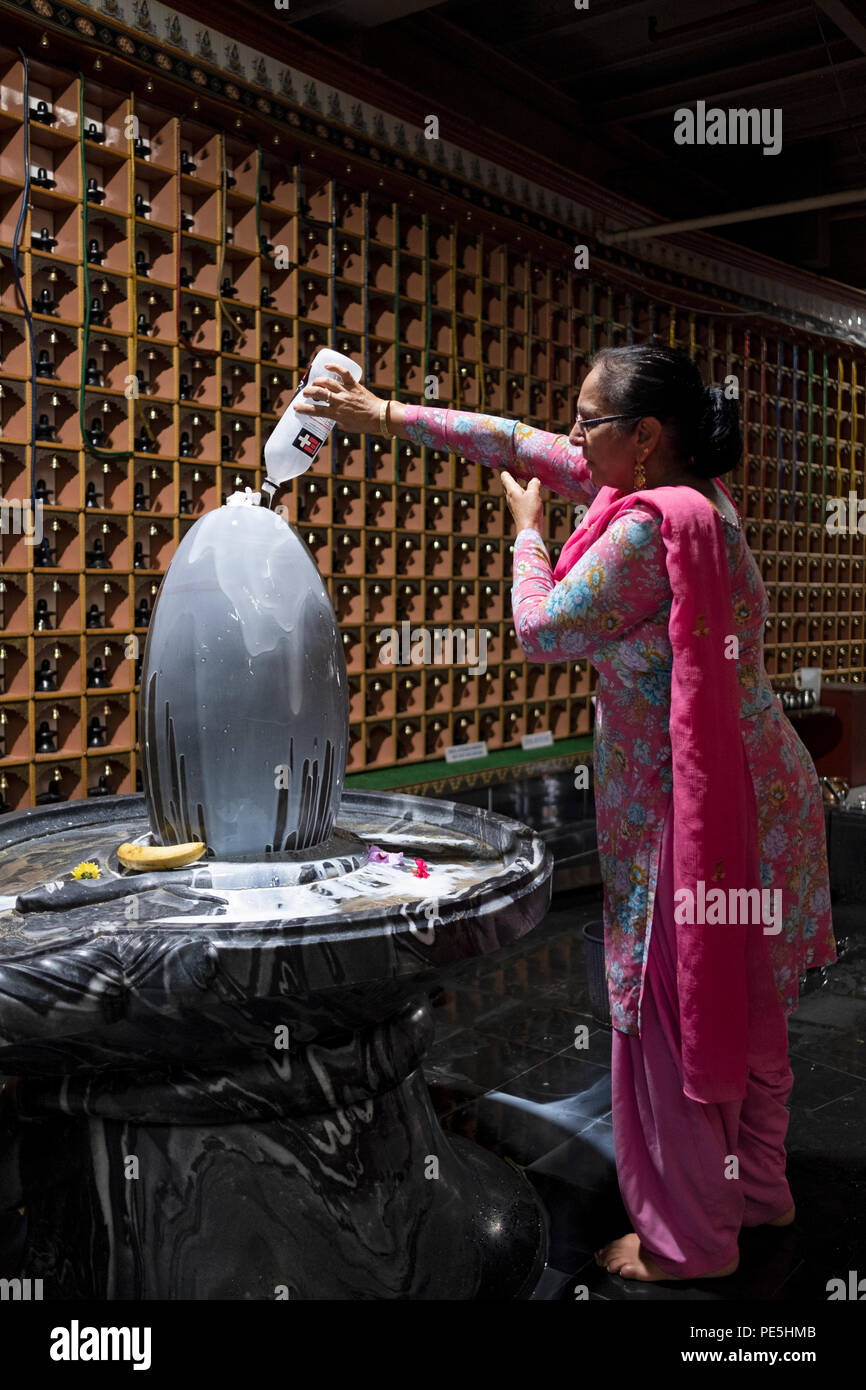 Eine Hindu-Frau gießt Milch über eine Statue des diessigen Shiva in einem Hindu-Tempel in Woodside, Queens New York City. Stockfoto