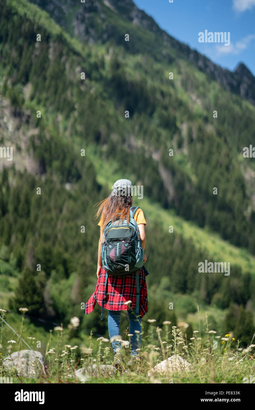 Junge Frau mit Rucksack steht auf einem Felsen mit erhobenen Händen und zu einem Tal unter suchen. Stockfoto