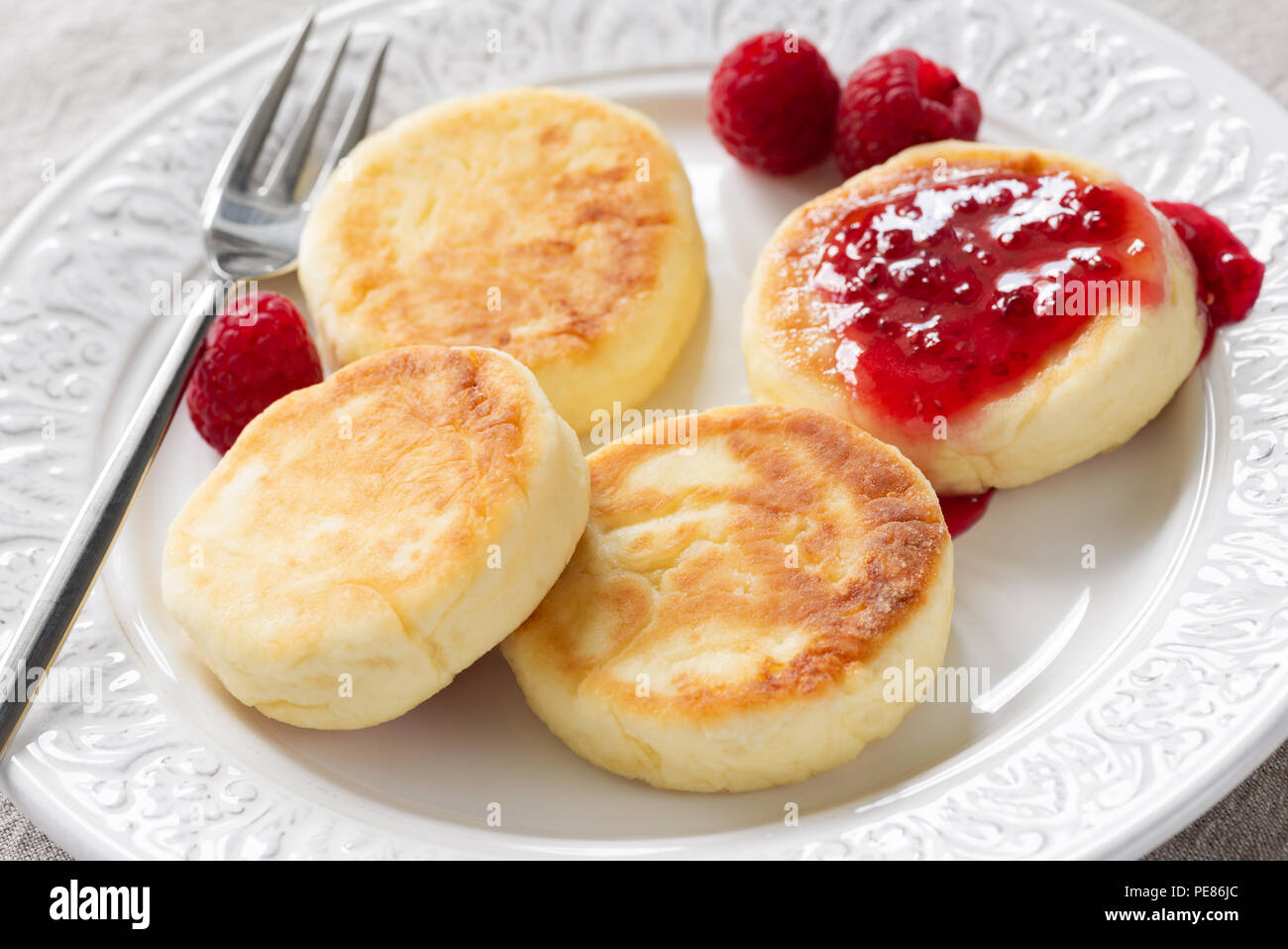 Quark Pfannkuchen oder syrniki mit himbeermarmelade auf weiße Platte, Detailansicht. Russische, ukrainische Küche. Gesund leckeres Frühstück Stockfoto