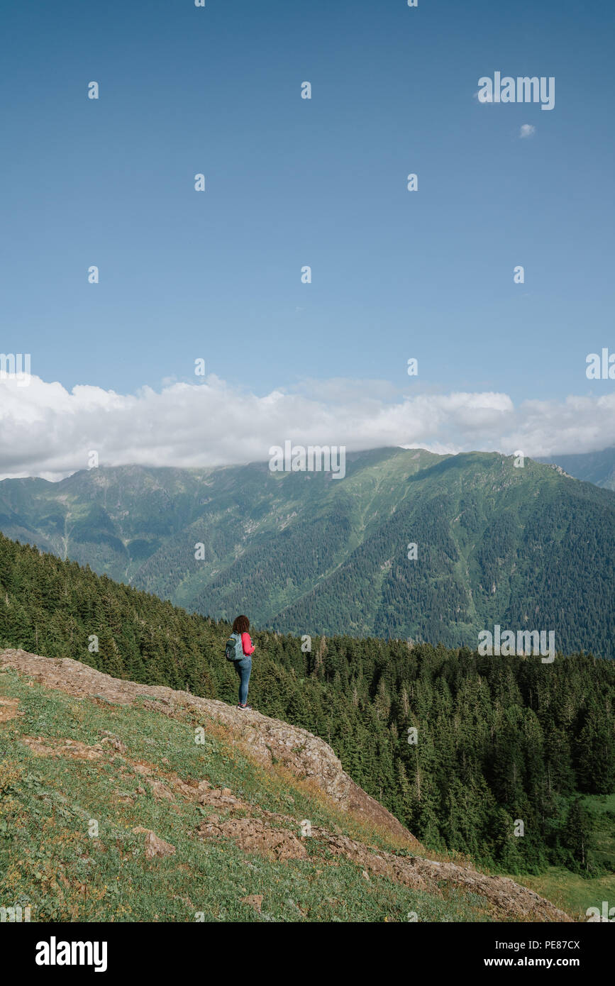 Junge Frau mit Rucksack, stehend auf einem Felsen zu einem Tal. Stockfoto