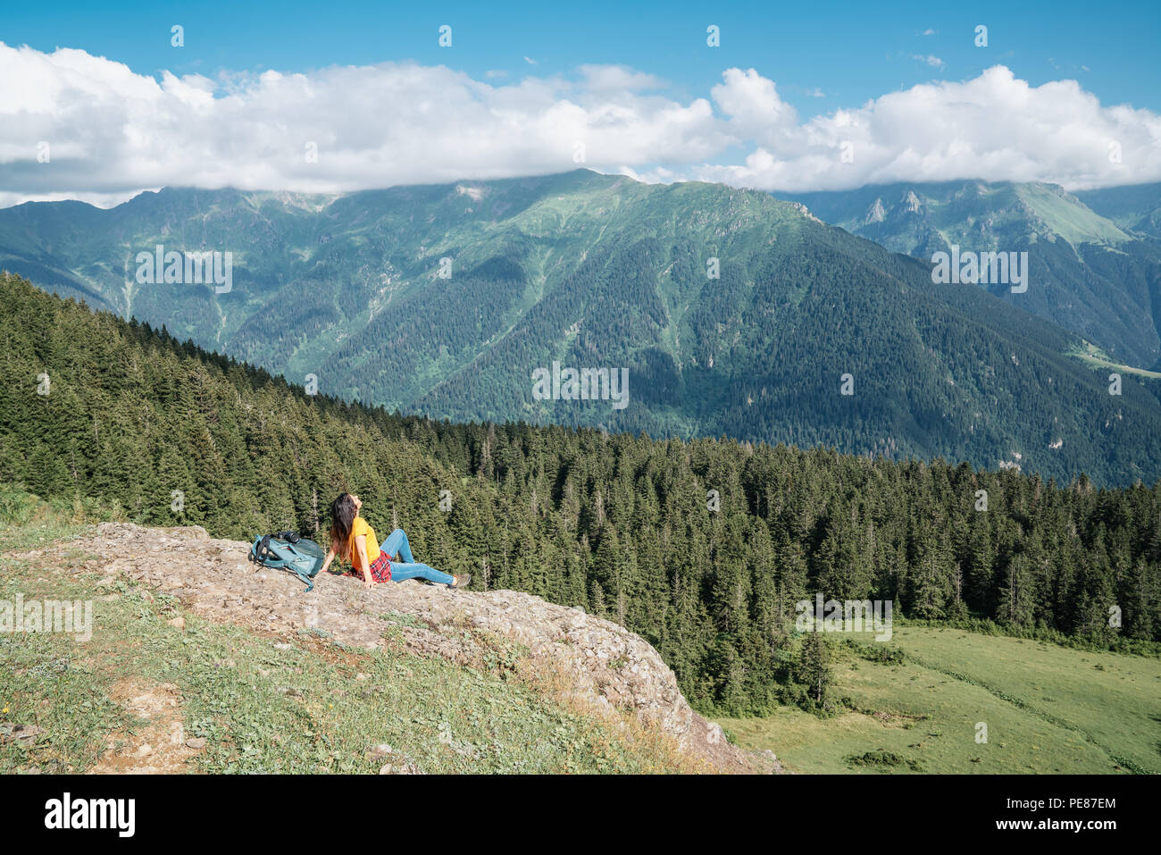 Junge Frau mit Rucksack, stehend auf einem Felsen zu einem Tal. Stockfoto