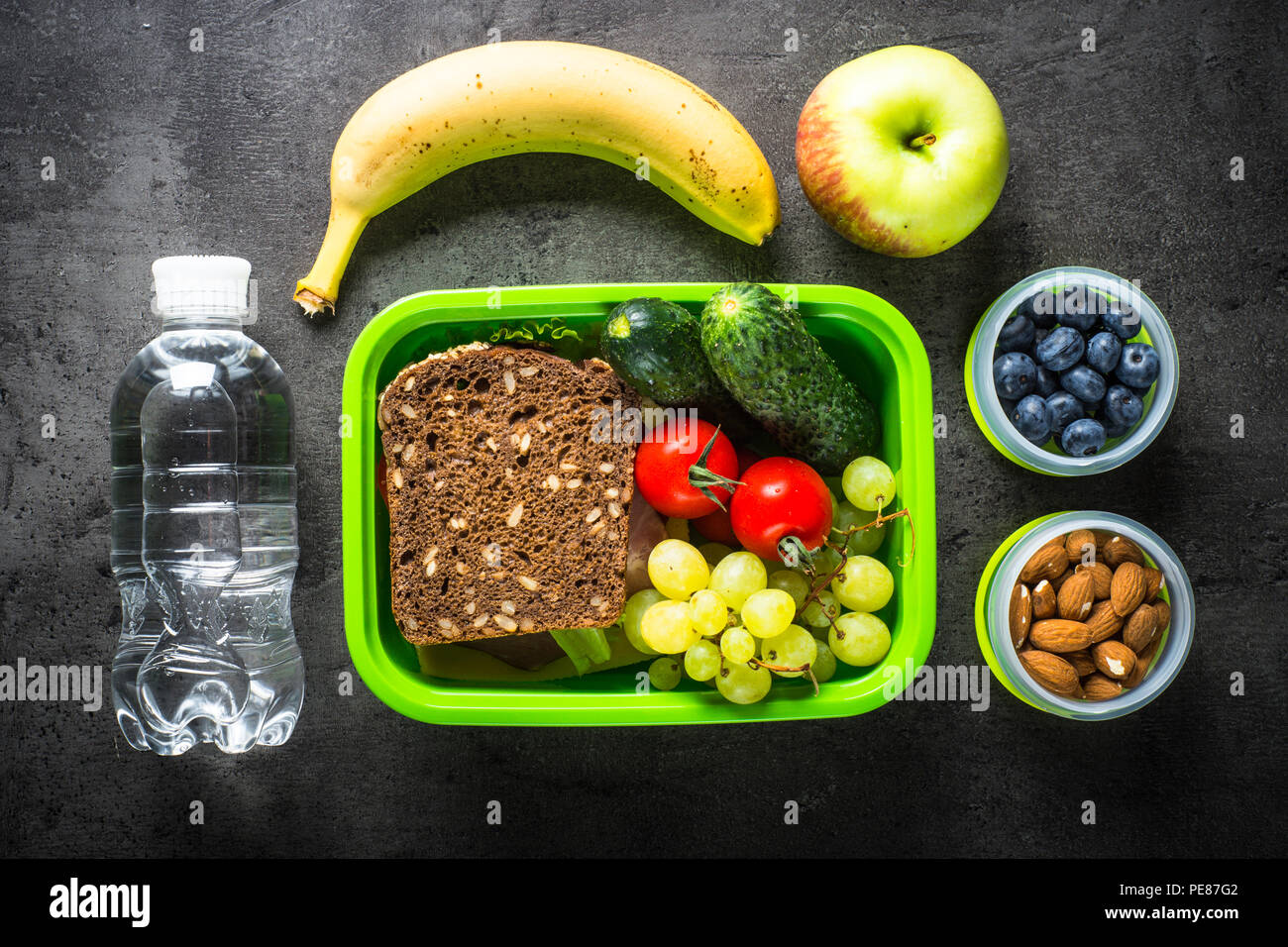 Lunch Box mit Sandwich, Gemüse, Bananen, Wasser, Nüsse und Beeren. Ansicht von oben mit der Kopie auf schwarzen Hintergrund. Stockfoto