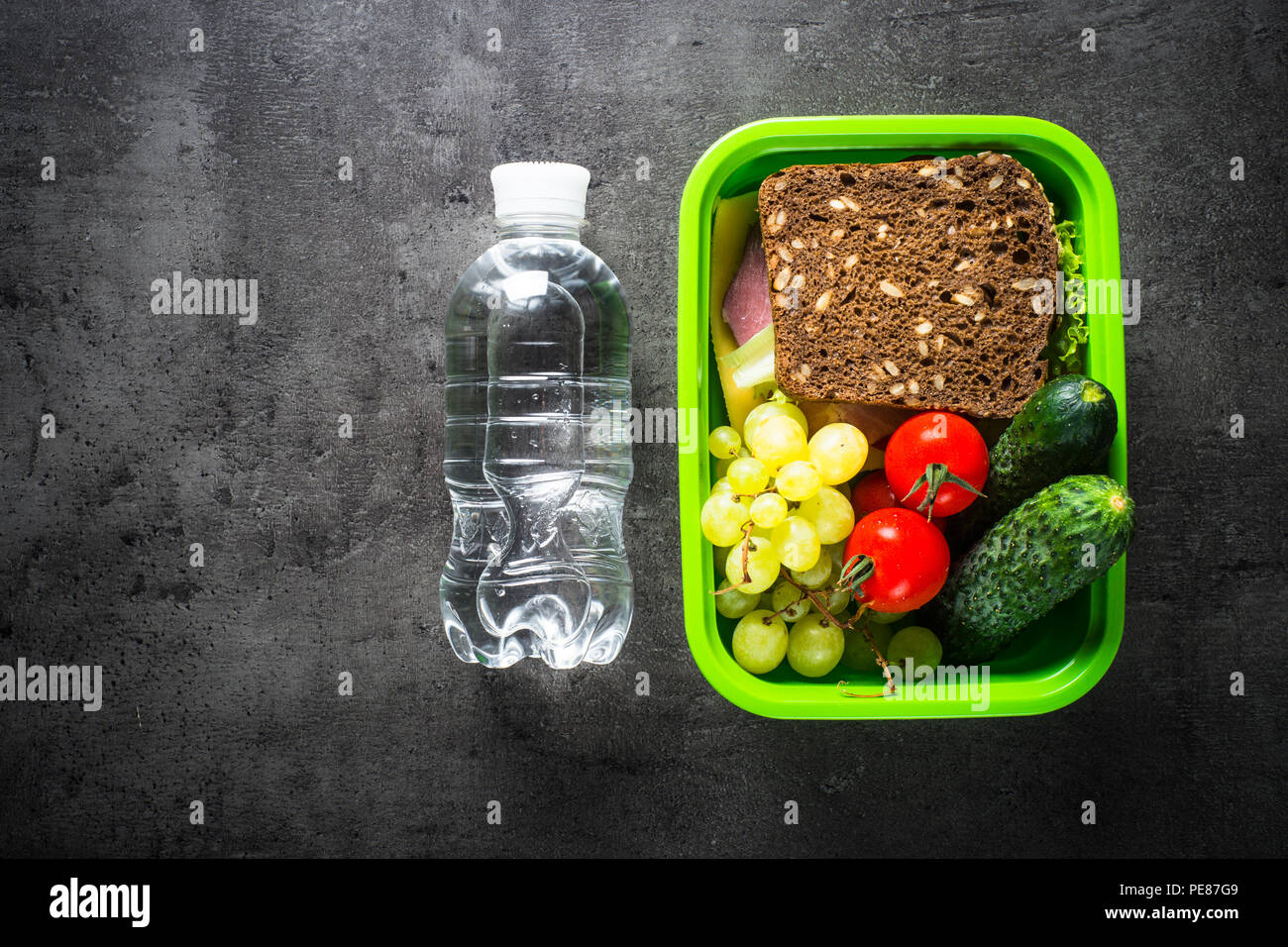 Lunch Box mit Sandwich, Obst und Wasser. Ansicht von oben mit der Kopie auf schwarzen Hintergrund. Stockfoto