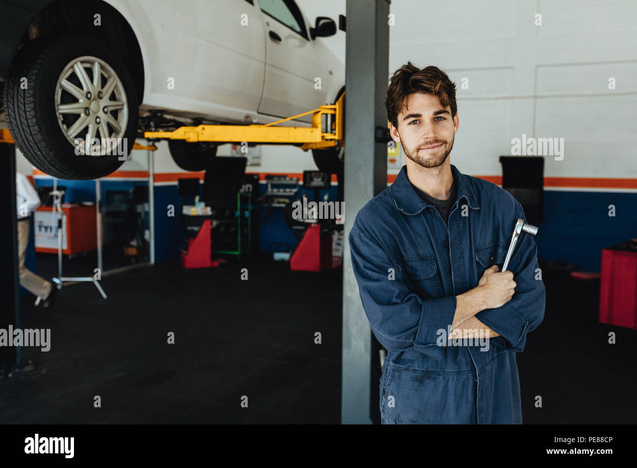 Junge Mechaniker stehen durch hydraulische Rampe in Garage. Mann in Uniform mit Spanner in der Automobil Service Station. Stockfoto