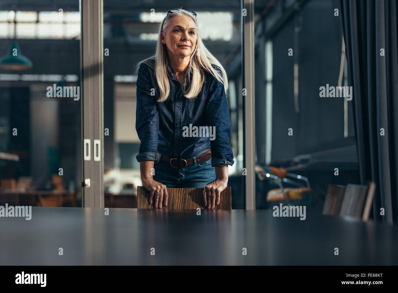 Portrait von erfolgreiche Geschäftsfrau gestützt auf einen Stuhl im Gemeinschaftsraum und Wegsehen. Ältere weibliche Unternehmer im Konferenzraum. Stockfoto