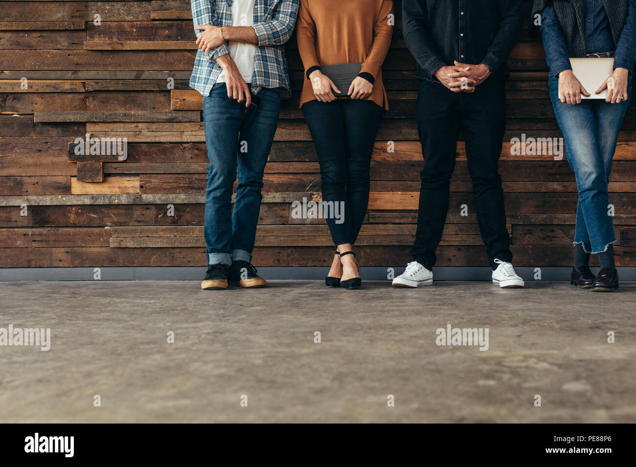 Untere Partie der Menschen gegen die Wand lehnt, bevor ein Job Interview mit Ordnern in die Hände in den Warteraum. Menschen in Reihe stehen Warten auf Jo Stockfoto