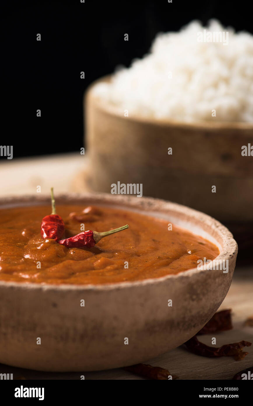 Nahaufnahme einer Schüssel mit einem Chicken Korma Curry und eine Schüssel mit gekochten Reis auf einem rustikalen Holztisch Stockfoto