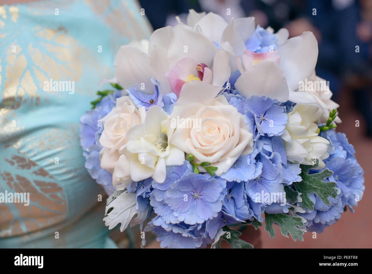 Kaukasischen jungen Brautjungfer oder weiblichen Gast trägt ein blaues Kleid mit silbernen Details und halten einen Strauß mit rosa Rosen, amdorchids Stockfoto