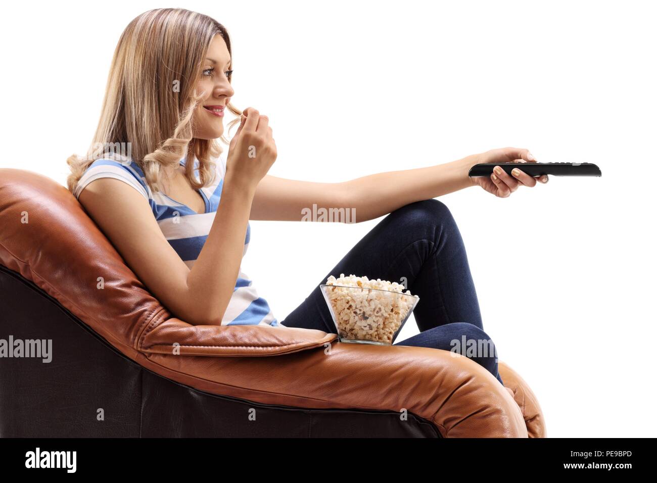 Junge Frau im Sessel vor dem Fernseher sitzen und essen Popcorn auf weißem Hintergrund Stockfoto