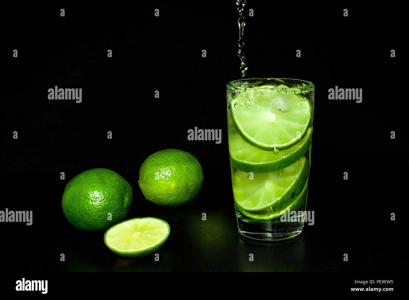 Kalte detox Wasser mit Eis und frischen Reifen Scheibe grün Limes auf schwarzem Hintergrund. Erfrischende Sommer und Getränke Konzept. Kalte detox Wasser mit Eis und Stockfoto