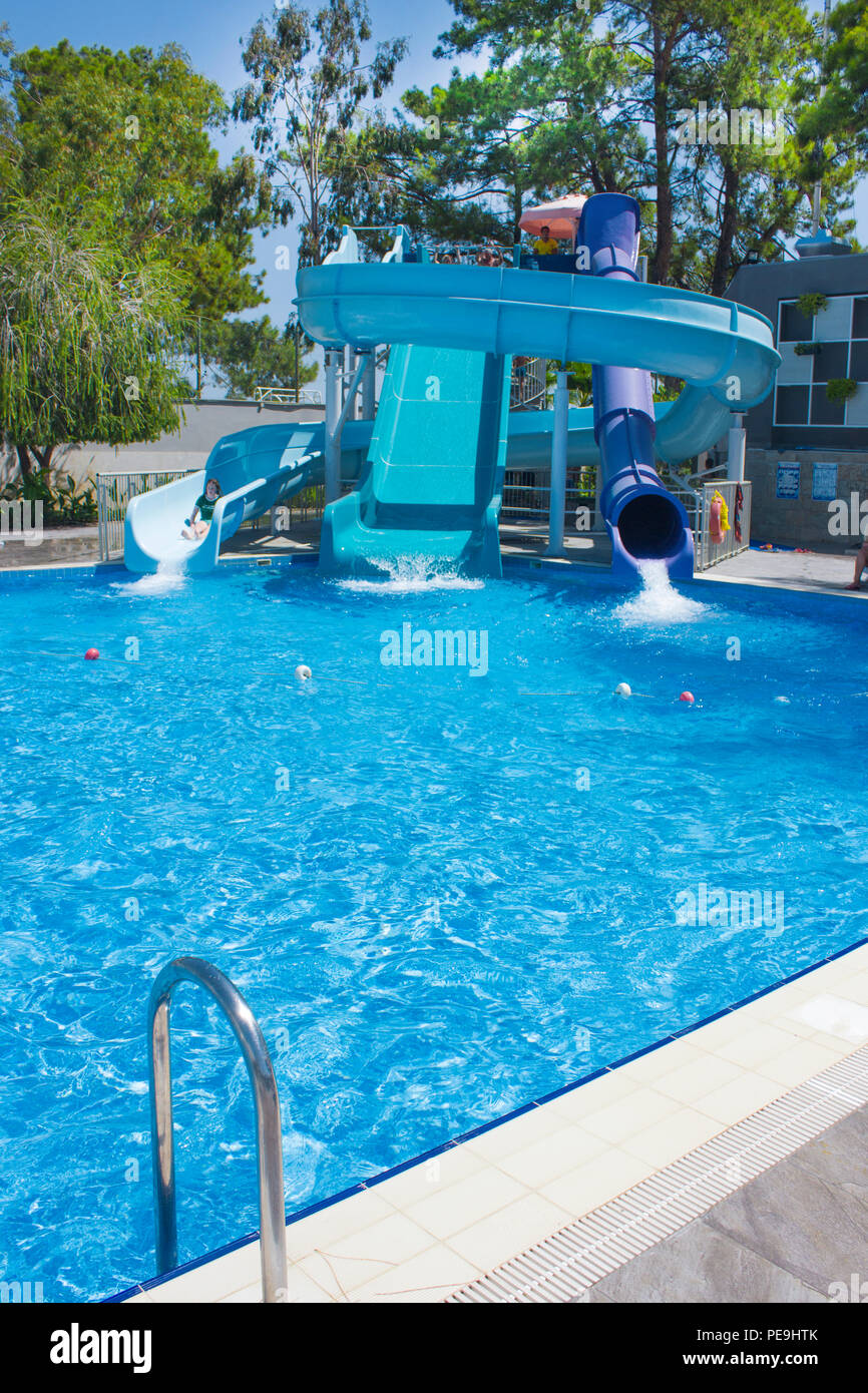 Großer Pool mit Wasserrutschen, unter blauem Himmel. Pinien im Hintergrund Stockfoto