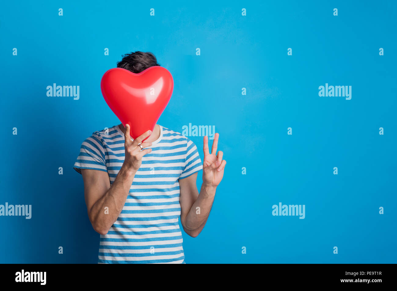 Porträt eines jungen Mannes in einem Studio auf einem blauen Hintergrund, mit roten Herzen. Stockfoto