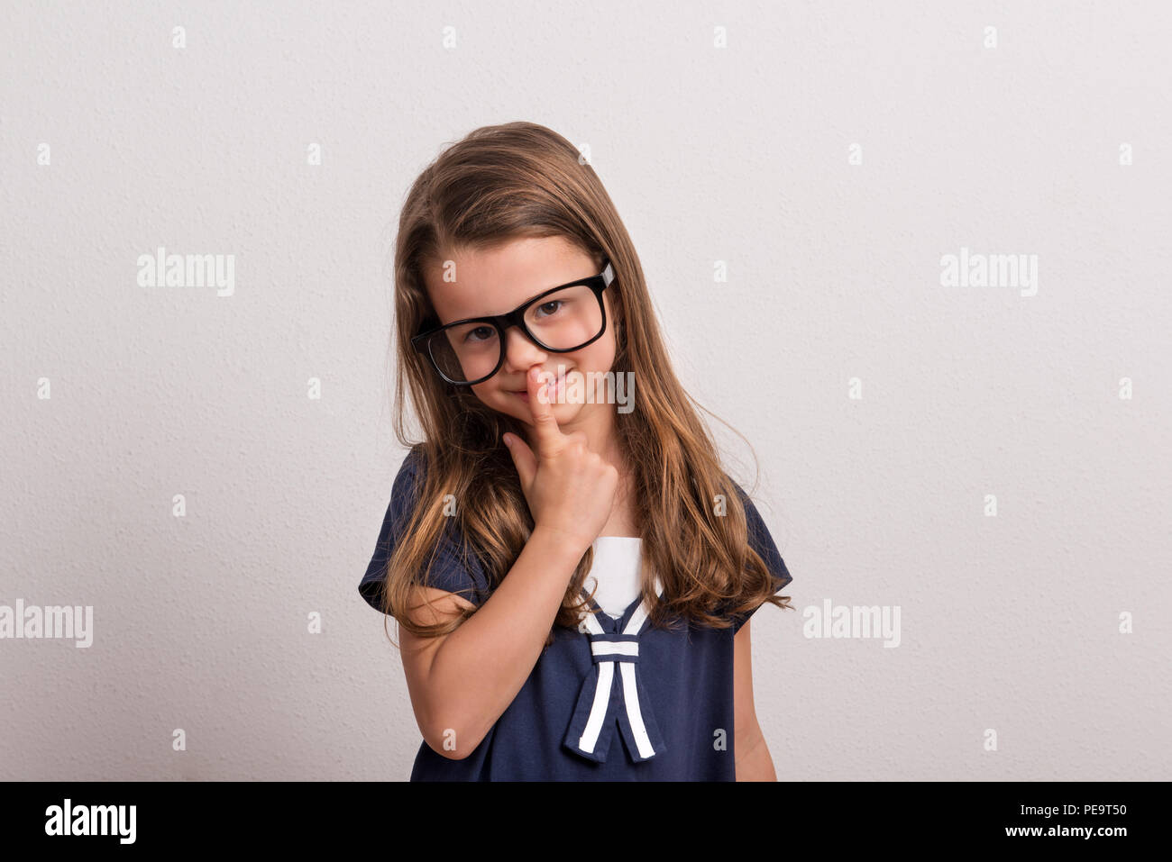 Porträt von einem kleinen Mädchen mit großen Brillen und einen Finger auf ihre Nase in ein Studio. Stockfoto