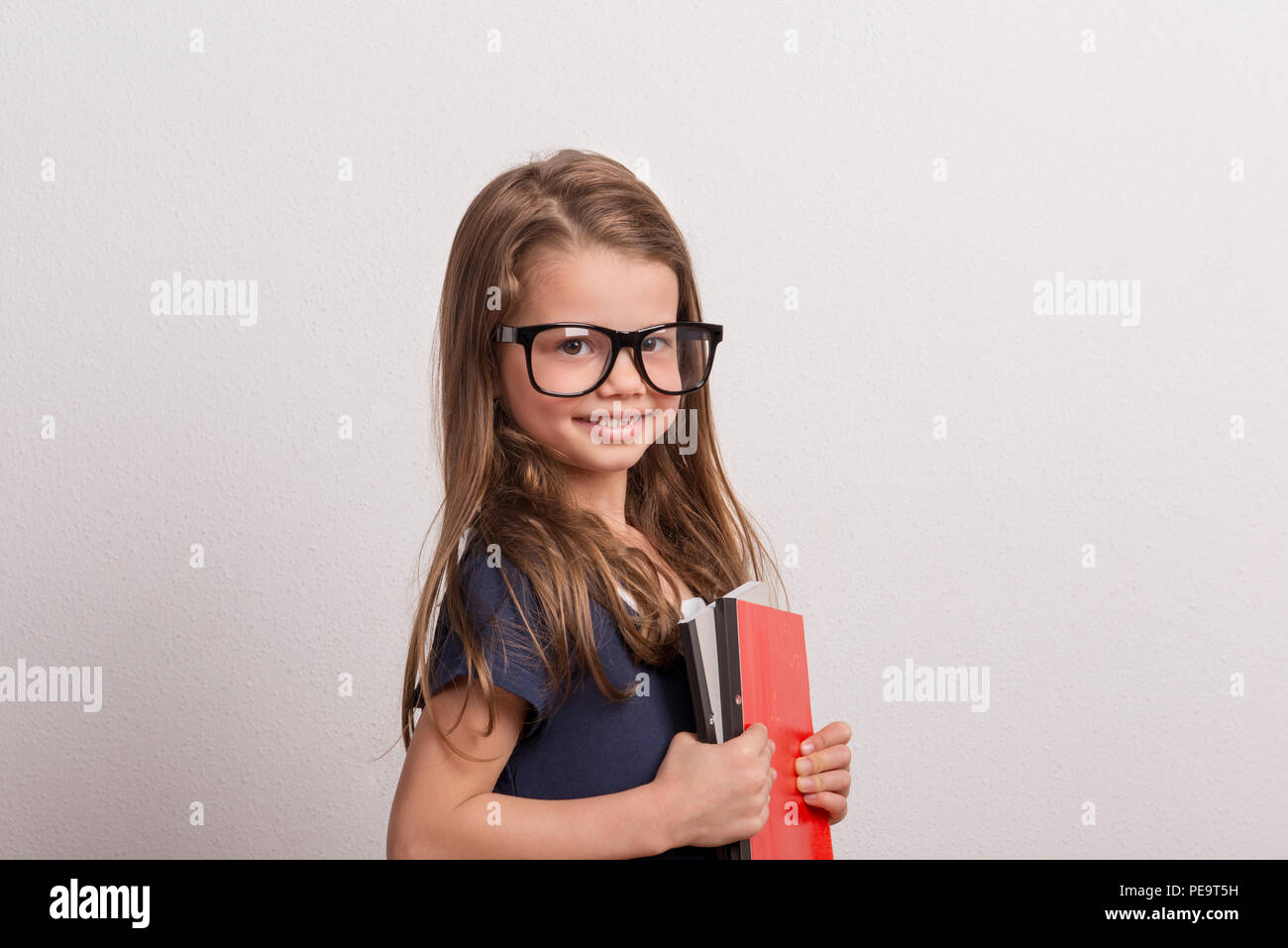 Porträt eines kleinen Schulmädchen mit große Gläser in einem Studio, Notebooks. Stockfoto