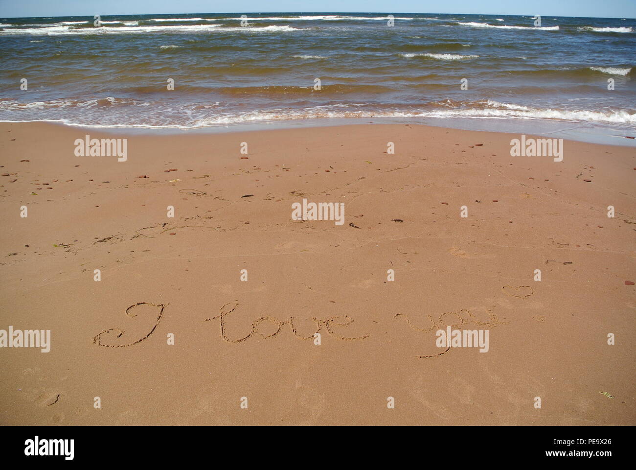 Die Worte "Ich liebe Dich" wunderschön handschriftlich auf dem roten Sand am Strand mit dem Himmel, Meer und Wellen im oberen Teil, Prince Edward Island Stockfoto