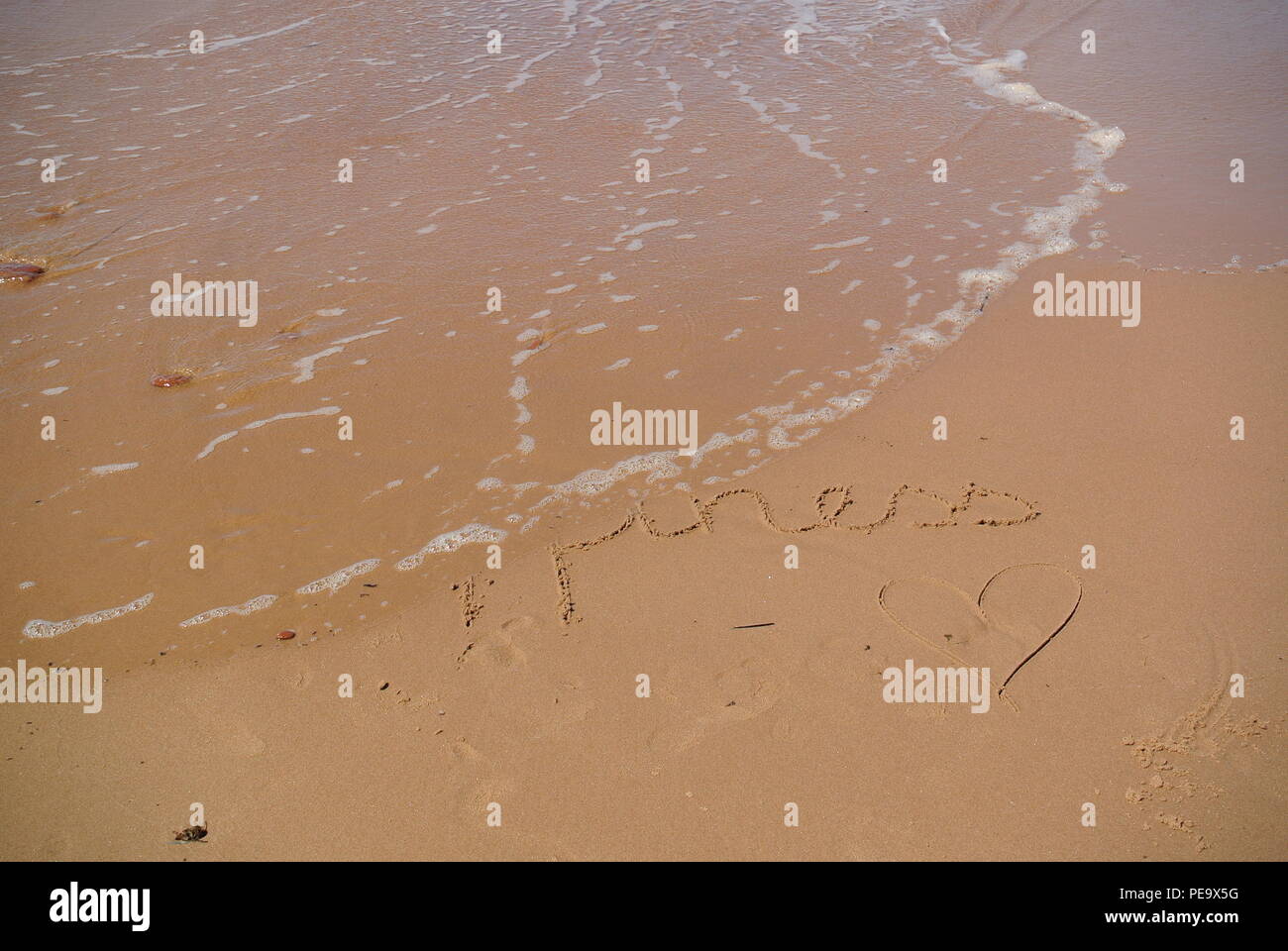 Verschwinden Wort "Glück" wunderschön handschriftlich auf dem roten Sand auf einem Strand mit einer Welle, die in der linken oberen Ecke, Prince Edward Island Stockfoto
